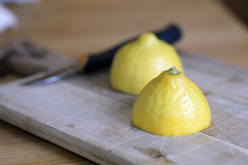 Cutting lemons - refreshing ingredient for cooking and baking. Closeup color image of the lemon, knife, cutting board and a wooden table surface. Healthy lifestyle image.