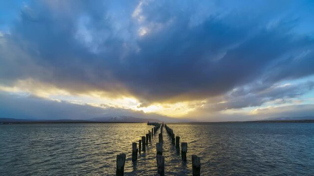 Timelapse serene view featuring the sun setting with a dramatic cloudy sky implied by a weathered pier leading into the water