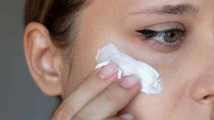 Close up of a young caucasian woman touching the face with her hand applying a smear of cream on...