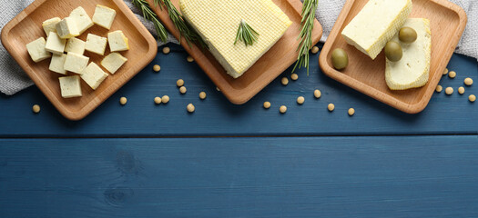 Delicious tofu, soybeans, olives and rosemary on blue wooden table, flat lay with space for text. Banner design