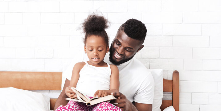 A father and daughter are sitting on a bed, reading a book together. The father is smiling and looking at the book, while the daughter is looking at the book with a thoughtful expression. - Powered by Adobe