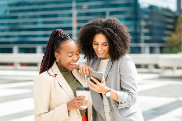 Two Businesswomen Discussing Project Ideas on Smartphone Outside Office Building