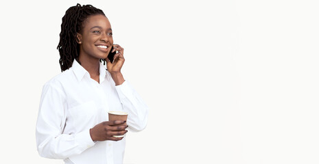 Cheerful young African American businesswoman wearing formal clothing talking on phone, holding...