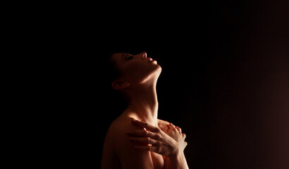 A black and white studio portrait of a womans head tilted back, looking up towards a light source....