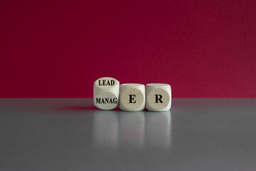 Turned a wooden cube and changes the word 'manager' to 'leader'. Beautiful pink background, gray table. Business and manager versus leader concept.