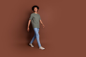 Fototapeta premium Full body length photo of youth guy with wavy hair in gray t shirt and jeans strolling outdoors isolated on brown color background