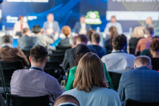 A diverse audience attentively listening to speakers during a professional conference or seminar. The event features a panel discussion and vibrant engagement.