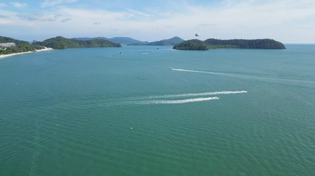 An aerial shot capturing the beauty of a tropical coastline with sea, boats, and a parasailer in the distance in Langkawi, Malaysia 