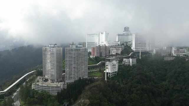Aerial View Of Modern high-rise buildings enveloped in fog, situated in a lush, mountainous region. The weather creates a serene and mysterious ambiance.