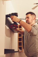 Handyman with battery drill fixing kitchen cabinets and shelf.