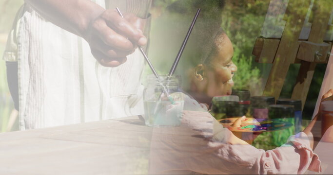 Image of african american woman painting on easel in garden