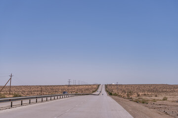 A long, empty road with no cars or people on it. The sky is clear and blue