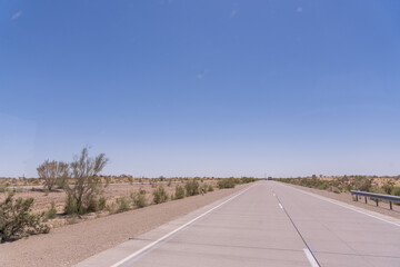 A road with a clear blue sky above it. The road is empty and there are no cars on it