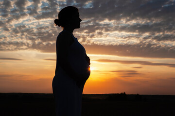Pregnant woman silhouette at sunset with a beautiful sky and clouds in the background