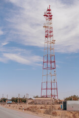 A tall red and white tower stands in the middle of a desert. The sky is clear and blue, and there are no clouds in sight. The tower is surrounded by a barren landscape