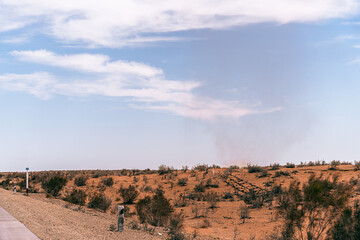 A desert landscape with a cloud in the sky. The sky is blue and the clouds are white