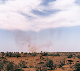 A desert landscape with a cloud in the sky. The sky is blue and the clouds are white