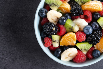 Fruit salad in a blue bowl on black background. Top view. Copy space