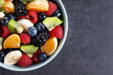 Fruit salad in a blue bowl on black background. Top view. Copy space