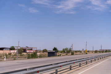 A deserted road with a few buildings in the distance. The sky is clear and blue. The road is empty and there are no cars or people on it