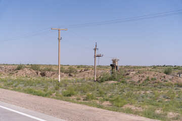 A rural area with a dirt road and a few trees. The sky is clear and blue