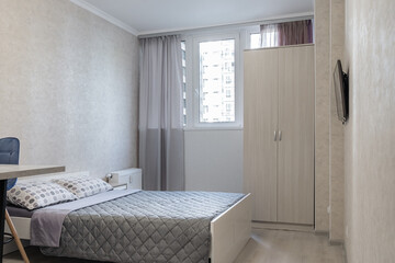 a bedroom with a big bed, a gray bedspread and pillows. There is a red and blue chair and a table near the bed.