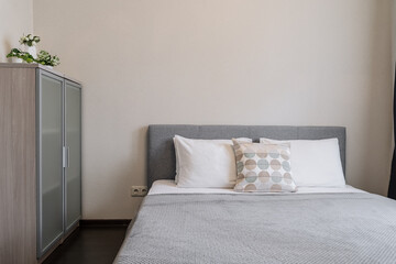 bedroom interior with a bed, grey bedspread, white pillows, grey chest of drawers and flowers