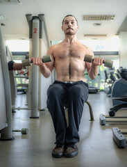 Naklejka premium Handsome muscular man pumps up his muscles lifting heavy dumbbell. Bodybuilder guy doing weightlifting exercise on bench in fitness gym. Young sport man workout strong bicep muscle by weight training.