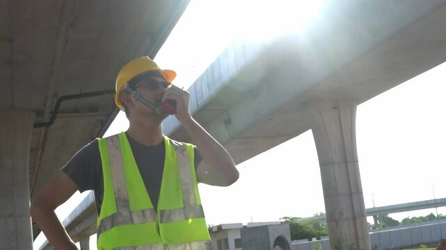 Asian male engineer using radio to inspect highway road bridge work