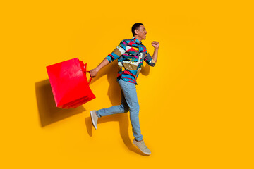 Full body photo of attractive young man running shopping bags dressed stylish colorful clothes isolated on yellow color background