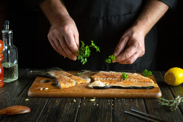 Cooking fish steak on the kitchen table with aromatic parsley and spices by the hands of the chef for lunch.
