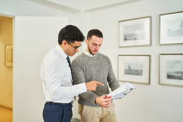 Two men are looking at a piece of paper, one pointing to it