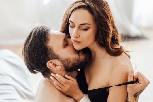 Sexy young undressed couple kissing with closed eyes sitting on the bed