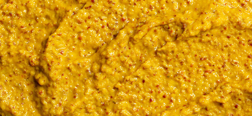 Mustard sauce with grains close-up. Hot spices as a background. Texture of Dijon mustard.