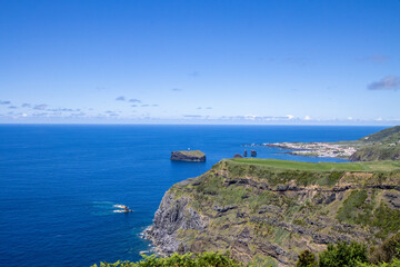 Expansive ocean view from a cliffside with clear blue water and bright sunlight reflecting on the surface.