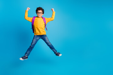 Full length photo of adorable little boy backpack jump winning schoolkid dressed stylish yellow garment isolated on blue color background