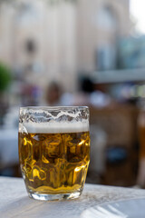 A glass of beer is sitting on a table. The glass is half full and has a frothy head. The scene takes place in a restaurant or bar, with people sitting at tables and chairs around the area