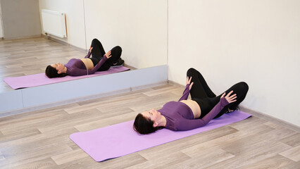 Athletic 30 woman practicing yoga lying on back on gym mat in Reclined Butterfly exercise relaxing...