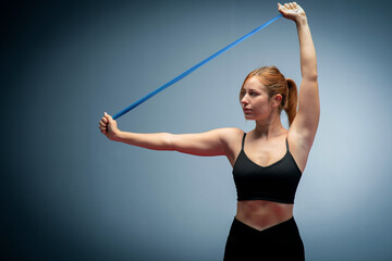 Fitness Girl In Fashion Sportswear. Woman in black sports clothes exercising with resistance band in studio.