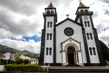 Fototapeta premium Ponta Delgada, White church with a clock tower under a bright sun and clear sky, with people walking nearby