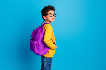 Photo portrait of small charming boy carry backpack turn around specs wear trendy yellow outfit isolated on blue color background
