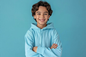 Happy Smiling Boy in Light Blue Hoodie with Arms Crossed Posing on Solid Background