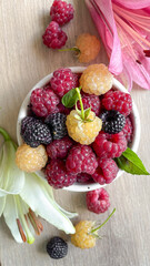raspberries of different varieties in a bowl on a light background with lily flowers, vitamins, fresh fruit, top view
