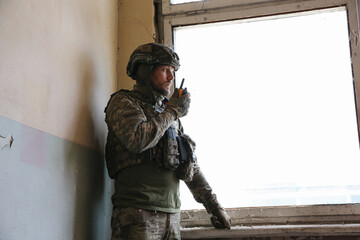 Military mission. Soldier in uniform with radio transmitter inside abandoned building, space for...