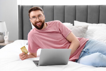 Online banking. Happy young man with credit card and laptop paying purchase at home