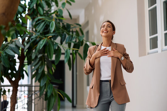 Happy businesswoman with eyes closed standing in office hallway. Copy space.