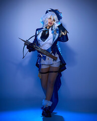 A girl in blue cosplay clothes, a wig and a crossbow poses in the studio against a background with blue lighting