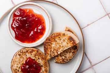 Hot Toasted Crumpets with piece of butter on a plate with strawberry jam. Perfect tasty breakfast popular in England, UK