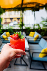 Hand holding a red cocktail garnished with strawberries and mint