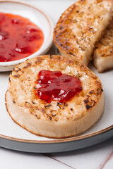 Hot Toasted Crumpets with piece of butter on a plate with strawberry jam. Perfect tasty breakfast popular in England, UK